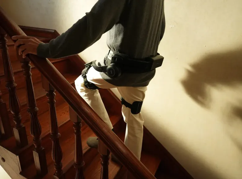 Osoba w egzoszkielecie AlpWalk S1 wchodzi po drewnianych schodach, trzymając się poręczy