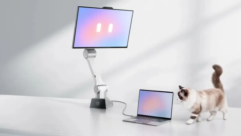 Monitor CyboPal ONE na białym robotycznym ramieniu na biurku, obok laptop i kot