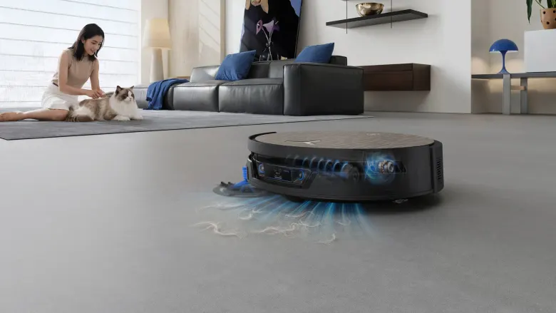 Robot DEEBOT X12S sprzątający szarą podłogę w salonie, w tle kobieta głaszcząca kota na dywanie