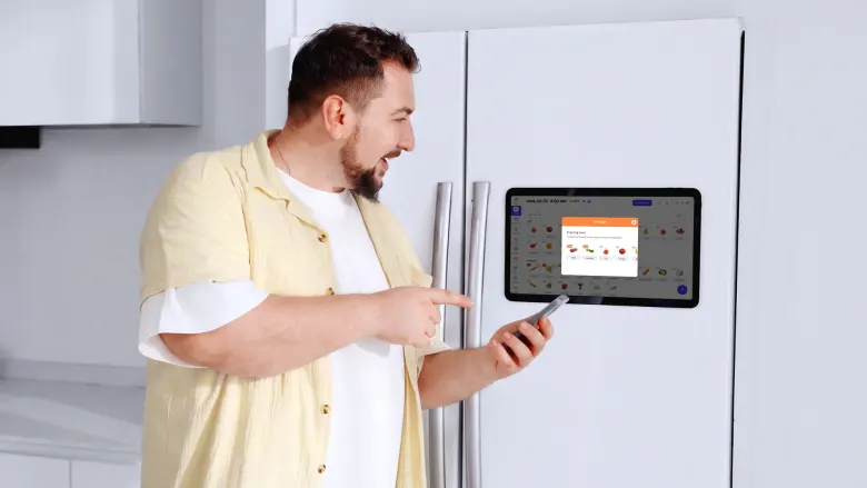 Mężczyzna z telefonem w ręku wskazuje listę produktów na ekranie Everblog FridgeCal 2