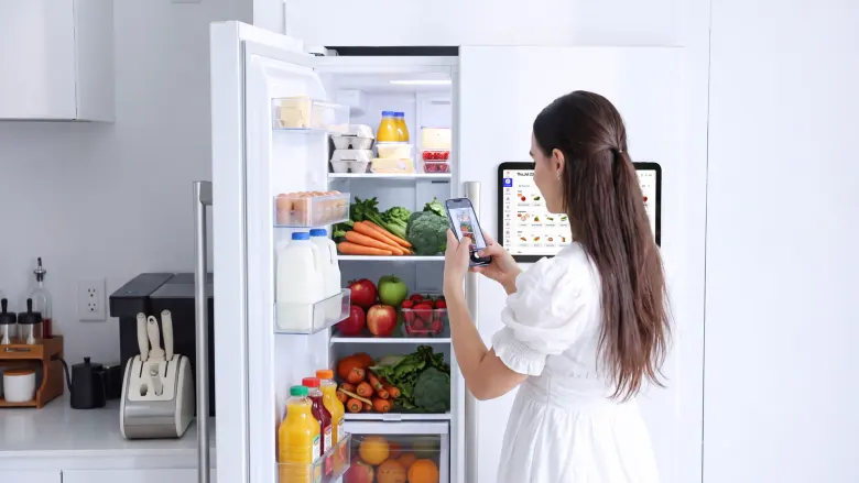 Kobieta robi smartfonem zdjęcie zawartości lodówki, obok na drzwiach wisi Everblog FridgeCal 2