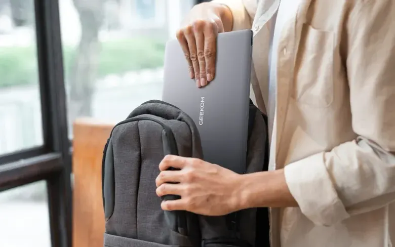 Osoba wkładająca szarego laptopa GEEKOM GeekBook X16 Pro do plecaka
