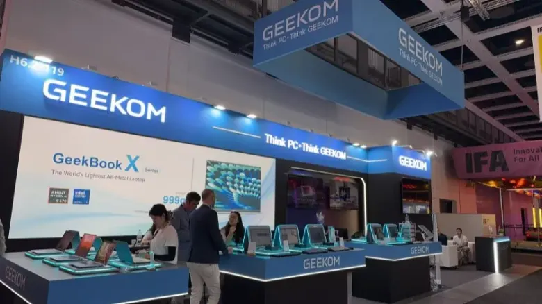Stoisko GEEKOM w hali 6.2 na IFA 2026 z laptopami GeekBook na ladzie i rozmawiającymi zwiedzającymi