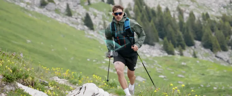 Turysta z kijkami trekkingowymi idzie górskim szlakiem, śledzony przez kamerę HOVERAir VERSA