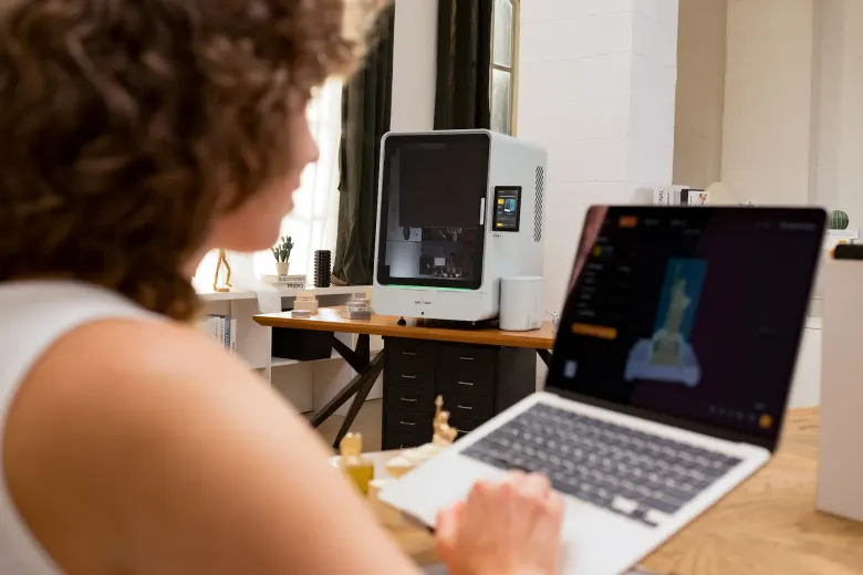 Użytkowniczka przygotowuje model w programie InfiStudio na laptopie, w tle frezarka InfiMaker K1