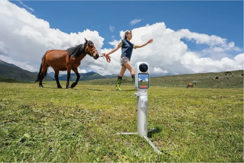 Kamera 360 Insta360 X6 na statywie nagrywa kobietę prowadzącą konia na łące