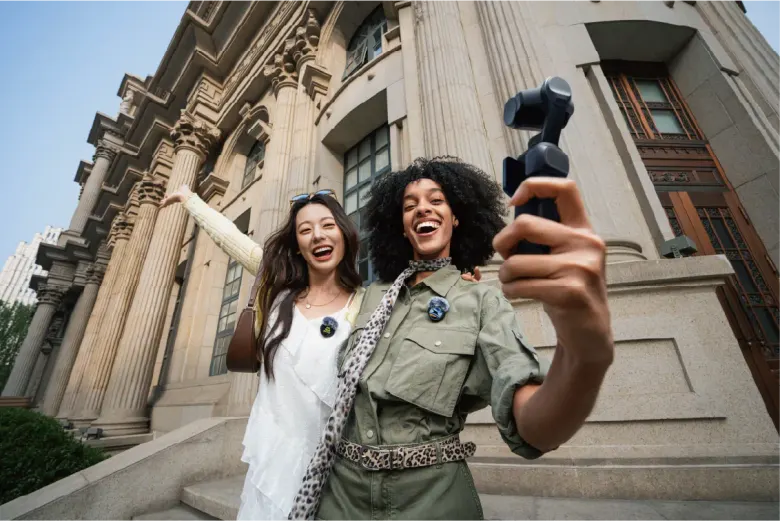 Dwie kobiety nagrywają vloga kamerą z gimbalem Insta360 Luna Ultra przed zabytkowym budynkiem