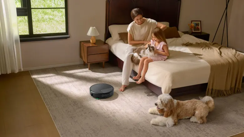 Roomba Max 875 Combo sprząta dywan w sypialni, obok kobieta z dzieckiem, kot i pies