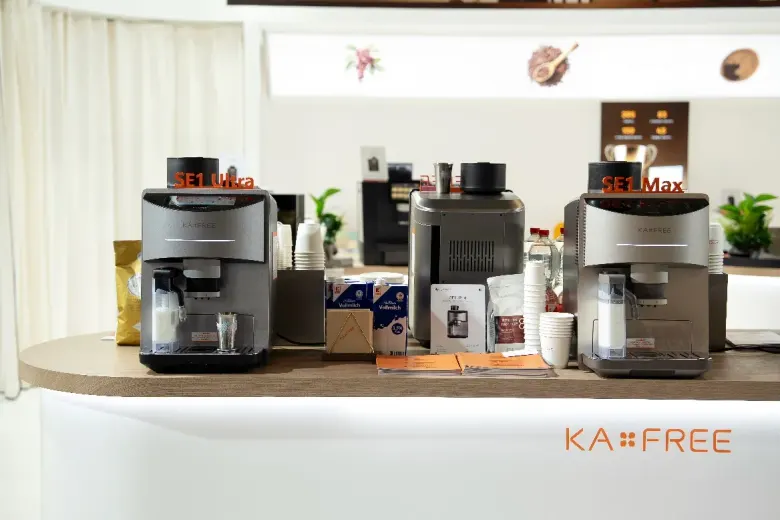 Automatyczne ekspresy KAXFREE na ladzie stoiska z kawą ziarnistą obok