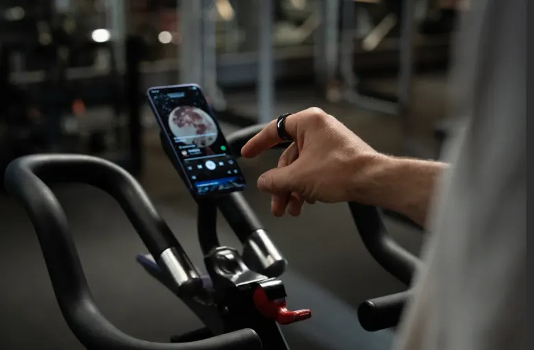 Rowerzysta z pierścieniem KiWear steruje odtwarzaniem muzyki na telefonie zamocowanym na rowerze stacjonarnym