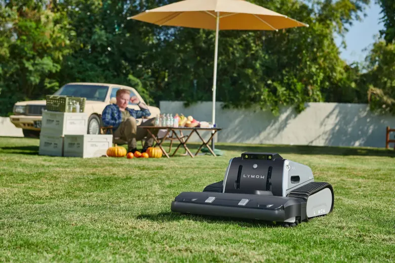 Robot koszący Lymow One Plus kosi trawnik, w tle mężczyzna odpoczywa pod parasolem