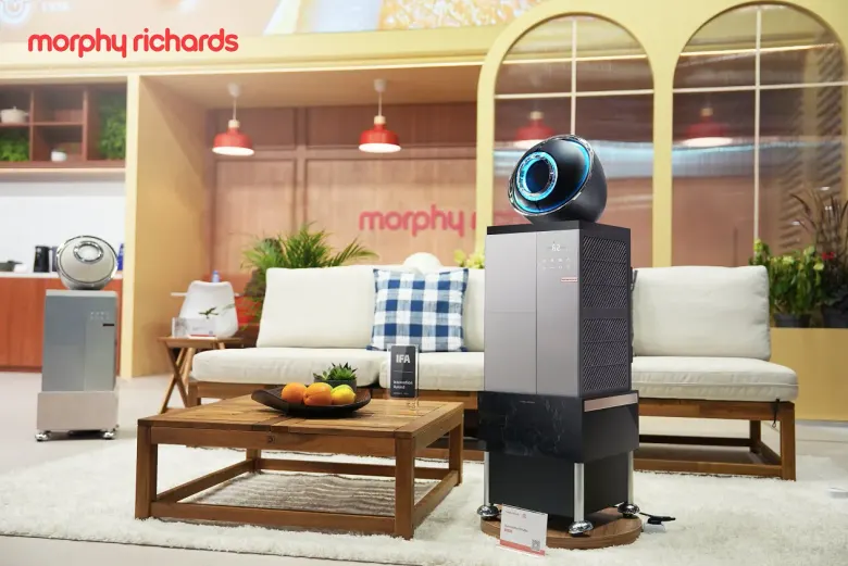 Stoisko Morphy Richards na IFA 2026 z ciemnym osuszaczem D1 Ultra przed kanapą i stolikiem