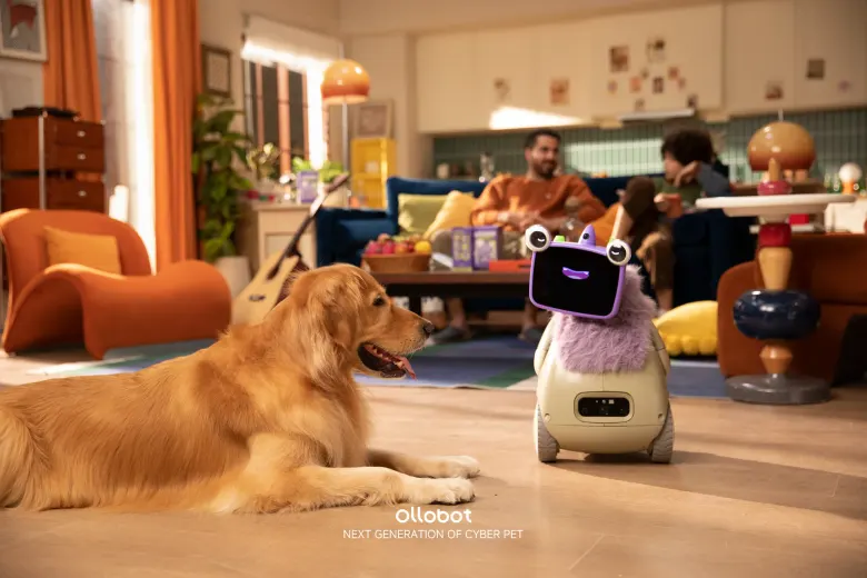Robot OlloNi SS1 w salonie obok psa golden retrievera, w tle rodzina na kanapie