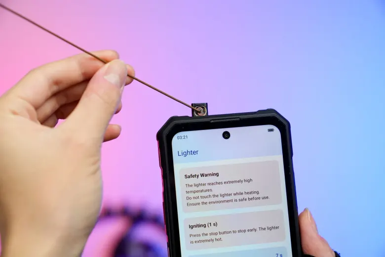 Oukitel WP63 z wysuniętą zapalniczką, od której ktoś odpala patyczek