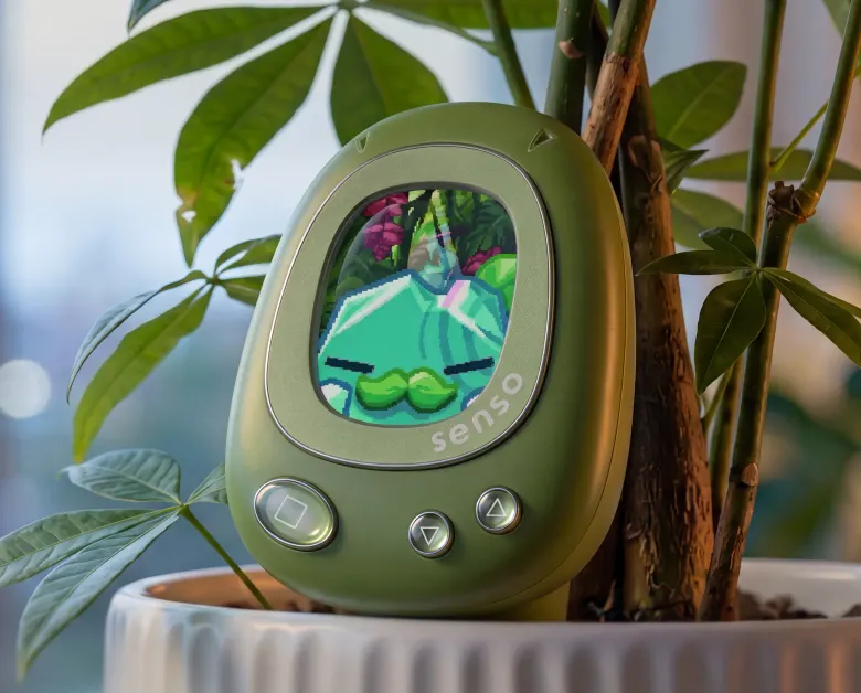 Zielony czujnik PlantSenso z pikselową postacią na ekranie wbity w doniczkę z rośliną