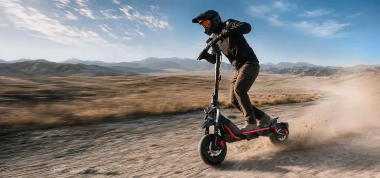 Rowerzysta w kasku jedzie hulajnogą Segway ZT3 MAX po szutrowej drodze, wzbijając kurz, w tle góry