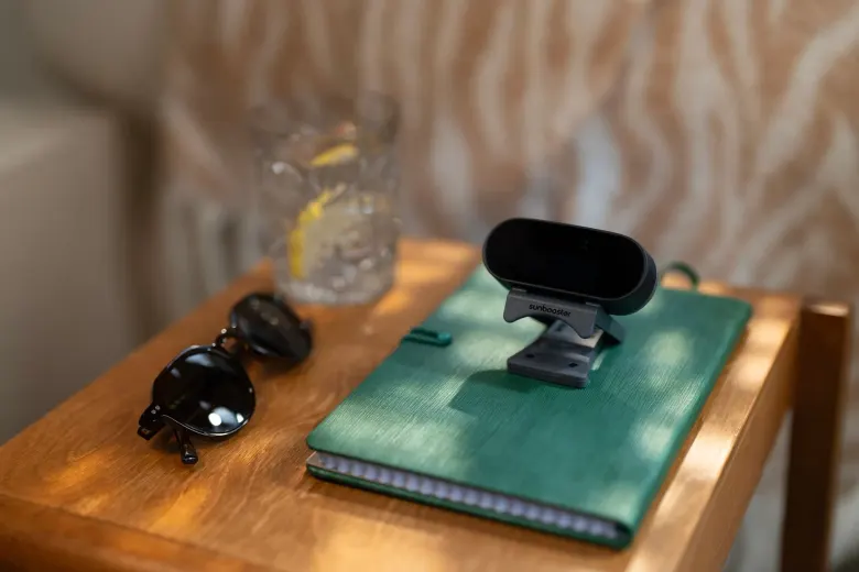 Lampa SunBooster stojąca na zielonym notesie na drewnianym stoliku obok okularów przeciwsłonecznych