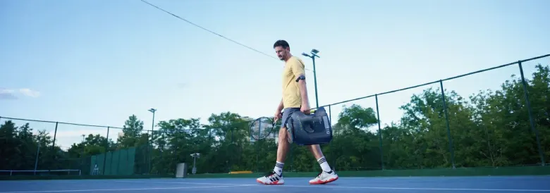 Tenisista niesie robota Tenniix w jednej ręce, a rakietę w drugiej, idąc po korcie