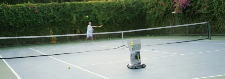 Tenisista odbiera piłkę zagraną przez robota Tenniix na ruchomej bazie po drugiej stronie siatki