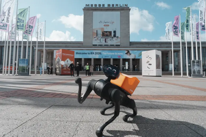 Czarny czworonożny robot Vbot z pomarańczowym plecakiem przed wejściem do Messe Berlin podczas IFA 2026