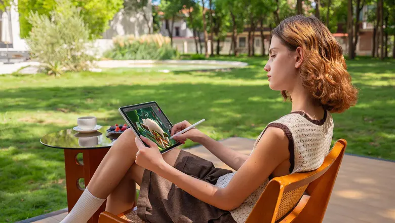 Kobieta rysuje rysikiem na tablecie XPPen Magic Pro 13, siedząc w ogrodzie
